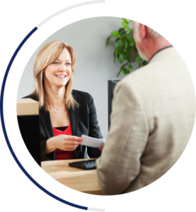 A smiling business woman in professional attire handing a check to a business man dressed in professional attire