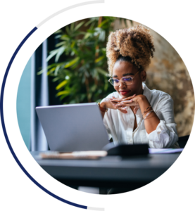 An image of a business woman in professional attire looking at her laptop screen. Her hands are clasped and she is resting her chin on them