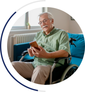 An image of an older man in a wheelchair wearing casual clothing. He is smiling while looking at his phone in his hand