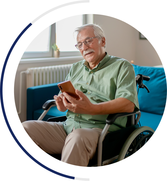 An image of an older man in a wheelchair wearing casual clothing. He is smiling while looking at his phone in his hand