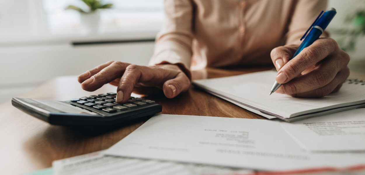 Close up of unrecognizable woman using calculator while going through bills and home finances.