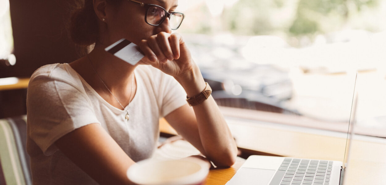 A person sitting on their laptop holding either a credit or debit card, prepared to make an online purchase